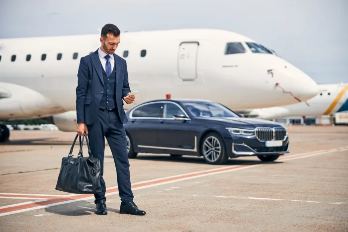 Business traveller booking an Excel Taxi Yeovil airport transfer by phone beside a car near the terminal